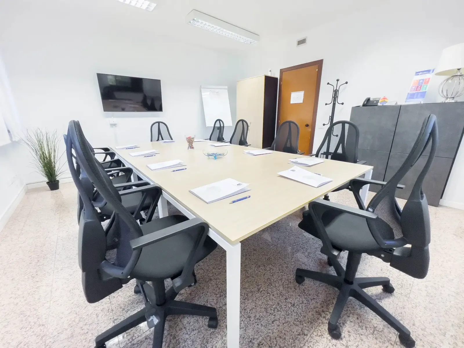 Sala riunioni con tavolo per otto persone e monitor a parete
